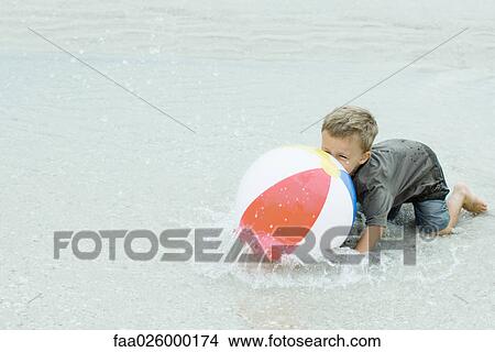 Little boy down on all fours in water, playing with beach ball View Large Photo Image Picture - Little boy down on all fours in water, playing with beach ball. Fotosearch