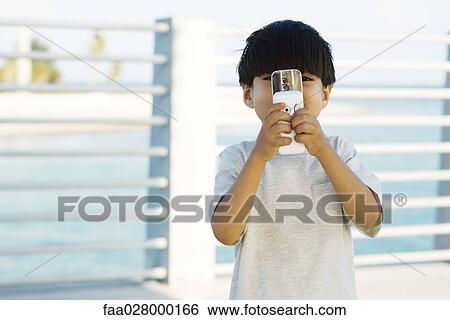 Stock Photograph - Little boy holding slide camera phone in front of face, front view. Fotosearch