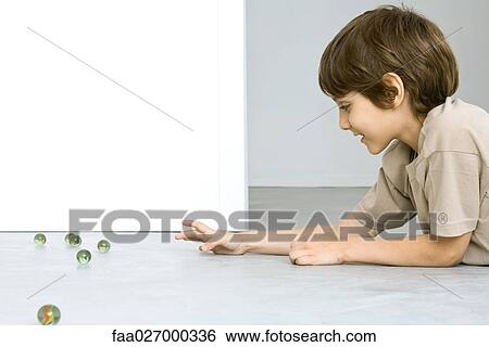 Little boy lying on the ground playing with marbles, side view View Large Photo Image Stock Photograph - Little boy lying on the ground playing with marbles, side view. Fotosearch
