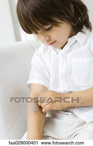 Little boy removing adhesive bandage from arm, looking down View Large Photo Image Stock Image - Little boy removing adhesive bandage from arm, looking down. Fotosearch