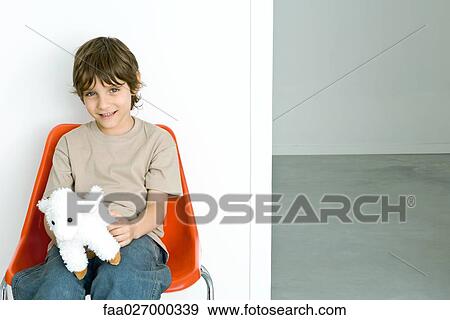 Little boy sitting in chair, holding stuffed toy, smiling on camera View Large Photo Image Stock Photo - Little boy sitting in chair, holding stuffed toy, smiling on camera. Fotosearch