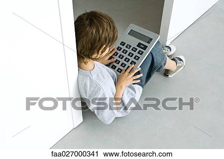 Stock Image - Little boy sitting on the ground, playing with large calculator, high angle view. Fotosearch