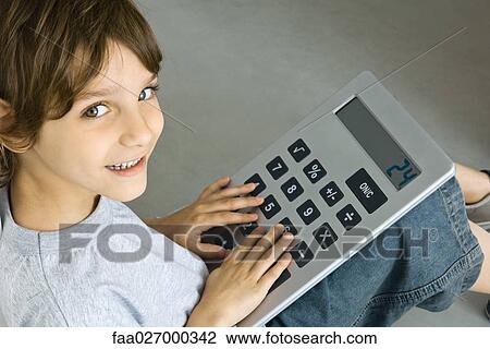 Stock Image - Little boy sitting on the ground, playing with large calculator, smiling at camera. Fotosearch