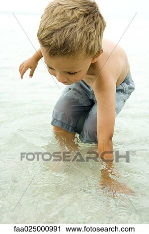 Little boy standing knee deep in ocean, bending over to put hand in water, close-up View Large Photo Image Stock Image - Little boy standing knee deep in ocean, bending over to put hand in water, close-up. Fotosearch