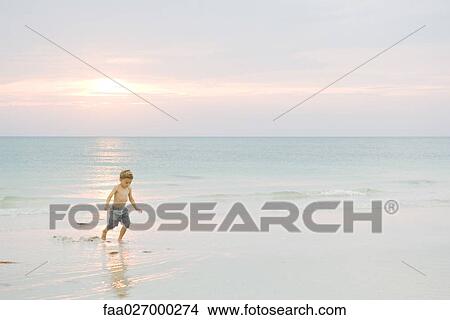 Little boy walking at the beach at sunset, looking down View Large Photo Image Picture - Little boy walking at the beach at sunset, looking down. Fotosearch