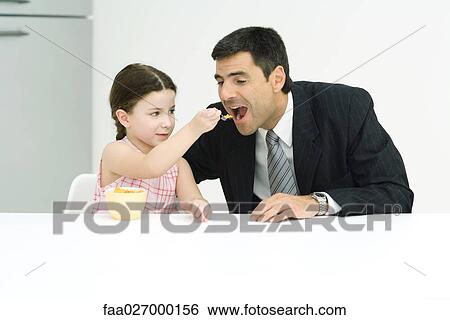 Little girl feeding cereal to her father, both sitting at table View Large Photo Image Stock Photograph - Little girl feeding cereal to her father, both sitting at table. Fotosearch