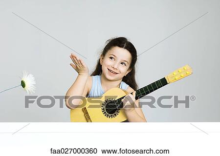 Little girl holding guitar, hand raised in gesture, smiling View Large Photo Image Stock Image - Little girl holding guitar, hand raised in gesture, smiling. Fotosearch