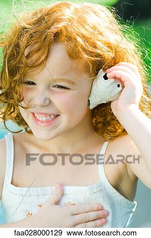 Little girl holding seashell up to ear, smiling, looking away View Large Photo Image Stock Photo - Little girl holding seashell up to ear, smiling, looking away. Fotosearch