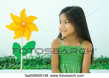 Stock Photo - Little girl looking at flower-shaped pinwheel, smiling. Fotosearch