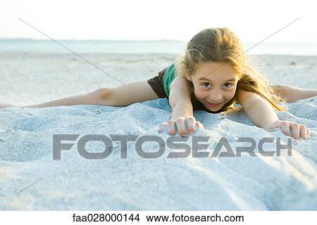 Little girl lying in sand at the beach, smiling at camera View Large Photo Image Picture - Little girl lying in sand at the beach, smiling at camera. Fotosearch