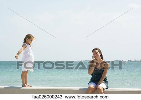 Little girl standing on low wall, watching older sister using cell phone View Large Photo Image Stock Image - Little girl standing on low wall, watching older sister using cell phone. Fotosearch