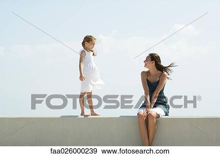 Little girl walking on ledge toward older sister, seated, both smiling at each other View Large Photo Image Stock Photo - Little girl walking on ledge toward older sister, seated, both smiling at each other. Fotosearch
