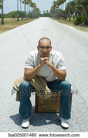 Stock Image - looking at camera, leaning on elbow, sitting, suitcase, road, hitchhiker. Fotosearch
