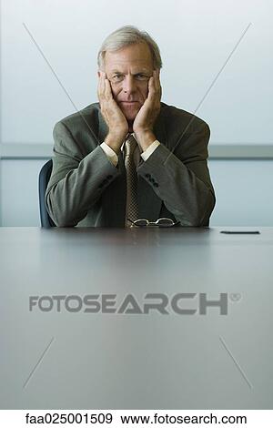 Stock Photo - looking at camera, leaning on elbow, businessman, holding head, ceo, hand under chin. Fotosearch