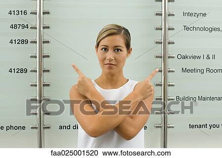 Stock Image - looking at camera, woman, number, wall, pointing, arms folded, in front of. Fotosearch