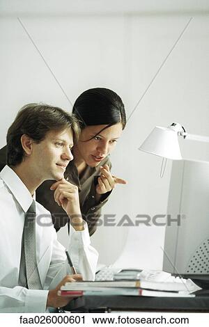 Stock Image - Male and female colleagues looking at computer together, woman pointing. Fotosearch