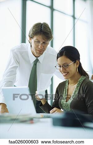 Male and female colleagues looking at laptop computer together, woman holding coffee cup View Large Photo Image Stock Image - Male and female colleagues looking at laptop computer together, woman holding coffee cup. Fotosearch