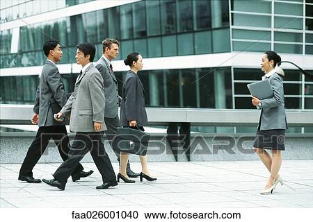 Stock Image - Male and female professionals walking on busy sidewalk, side view. Fotosearch