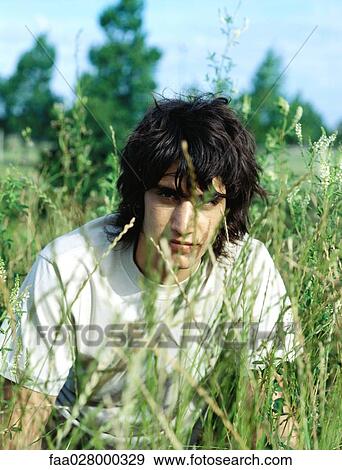 Stock Photo - Male crouching in tall grass, looking at camera, portrait. Fotosearch
