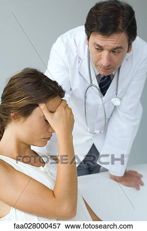 Stock Photo - Male doctor examining patient, woman sitting with hand over eyes. Fotosearch