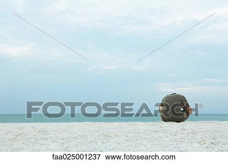 Male sitting on beach with head down, rear view View Large Photo Image Stock Photo - Male sitting on beach with head down, rear view. Fotosearch