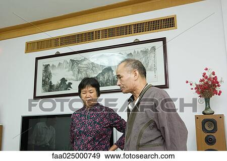 Stock Photo - Man and woman standing together in living room, looking away. Fotosearch