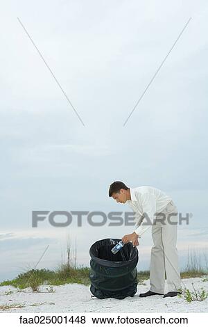 Man at the beach, placing water bottle in garbage can View Large Photo Image Stock Photo - Man at the beach, placing water bottle in garbage can. Fotosearch