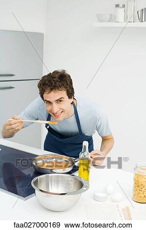 Man cooking in kitchen, bending over to taste sauce, smiling at camera View Large Photo Image Stock Photo - Man cooking in kitchen, bending over to taste sauce, smiling at camera. Fotosearch