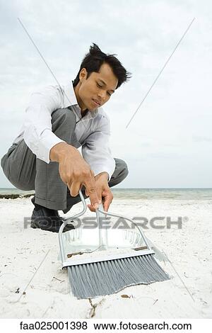 Man crouching on beach, sweeping sand into dustpan, low angle view View Large Photo Image Stock Photo - Man crouching on beach, sweeping sand into dustpan, low angle view. Fotosearch