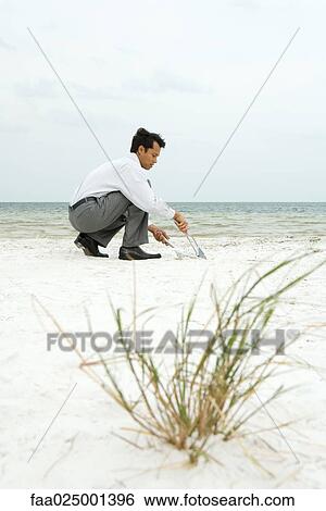 Man crouching on beach, sweeping sand into dustpan, side view View Large Photo Image Stock Photograph - Man crouching on beach, sweeping sand into dustpan, side view. Fotosearch