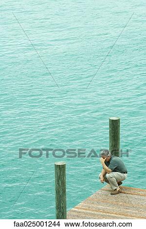 Man crouching on dock, holding head, high angle view View Large Photo Image Picture - Man crouching on dock, holding head, high angle view. Fotosearch