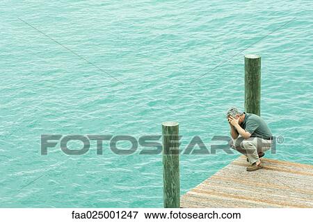 Man crouching on dock, holding head, high angle view View Large Photo Image Stock Photo - Man crouching on dock, holding head, high angle view. Fotosearch