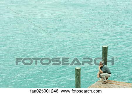 Man crouching on dock, holding head, high angle view View Large Photo Image Stock Photograph - Man crouching on dock, holding head, high angle view. Fotosearch