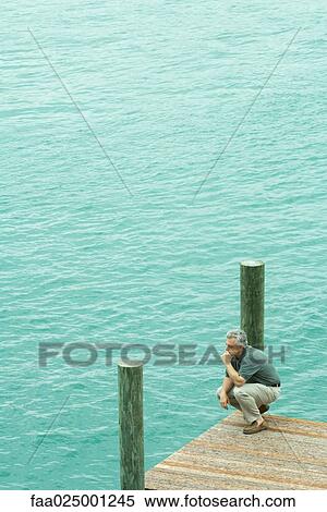 Man crouching on dock, holding head, high angle view View Large Photo Image Stock Photography - Man crouching on dock, holding head, high angle view. Fotosearch