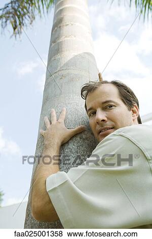 Man embracing tree, looking over shoulder at camera, low angle view View Large Photo Image Stock Photo - Man embracing tree, looking over shoulder at camera, low angle view. Fotosearch
