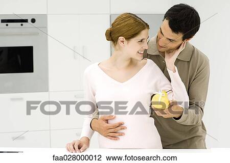 Stock Image - Man giving woman pear tied with ribbon, both smiling. Fotosearch