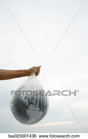 Stock Photograph - Man holding globe in plastic bag, cropped view. Fotosearch