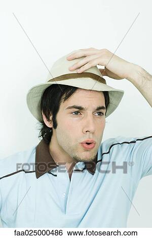 Man holding hat on head, looking away, puckering lips View Large Photo Image Stock Photograph - Man holding hat on head, looking away, puckering lips. Fotosearch