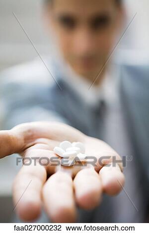 Stock Image - Man holding out handful of pills, cropped view, selective focus. Fotosearch