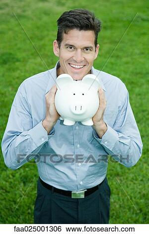 Man holding piggy bank under chin, smiling at camera View Large Photo Image Stock Photograph - Man holding piggy bank under chin, smiling at camera. Fotosearch