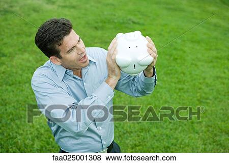 Man holding piggy bank upside down, looking surprised View Large Photo Image Stock Photo - Man holding piggy bank upside down, looking surprised. Fotosearch