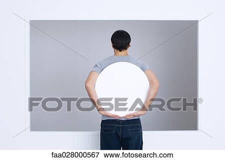Stock Photo - Man holding round sign behind back, rear view. Fotosearch