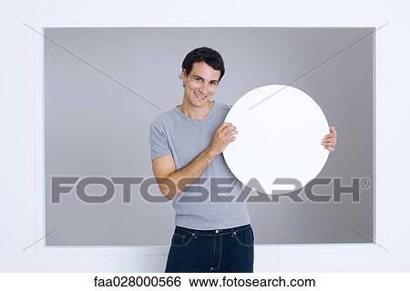 Stock Photograph - Man holding up round sign, smiling at camera. Fotosearch