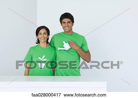 Man holding watering can, standing beside woman wearing tee-shirt printed with plant graphic, portrait View Large Photo Image Stock Photo - Man holding watering can, standing beside woman wearing tee-shirt printed with plant graphic, portrait. Fotosearch