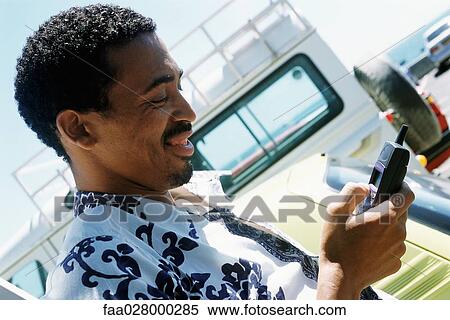 Man in Hawaiian shirt outdoors, looking down at cell phone, smiling View Large Photo Image Stock Photography - Man in Hawaiian shirt outdoors, looking down at cell phone, smiling. Fotosearch