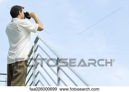 Man leaning against railing, looking through binoculars View Large Photo Image Stock Photo - Man leaning against railing, looking through binoculars. Fotosearch