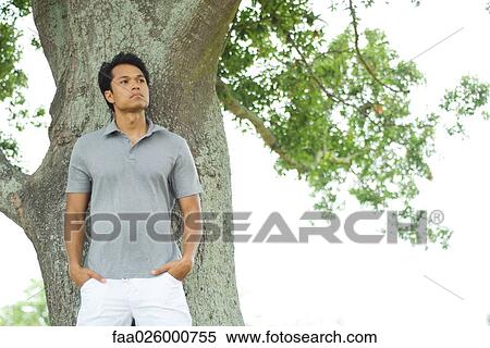 Man leaning against tree, looking away, three quarter length View Large Photo Image Stock Photography - Man leaning against tree, looking away, three quarter length. Fotosearch
