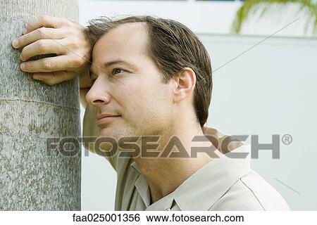 Man leaning against tree trunk, looking away, close-up View Large Photo Image Stock Photograph - Man leaning against tree trunk, looking away, close-up. Fotosearch