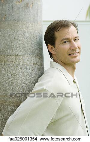 Picture - Man leaning against tree trunk, smiling over shoulder at camera. Fotosearch