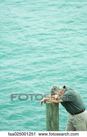 Man leaning on post, head down on arms, high angle view, water in background View Large Photo Image Stock Image - Man leaning on post, head down on arms, high angle view, water in background. Fotosearch